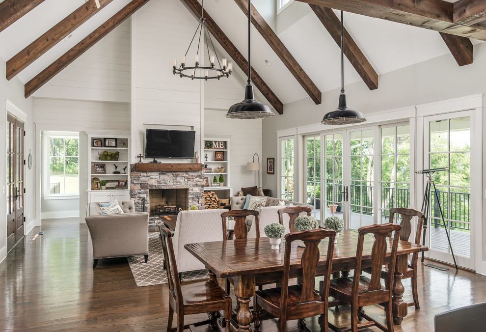 Exemple d'une salle à manger ouverte sur le salon nature avec un mur beige, un sol en bois brun, une cheminée standard, un manteau de cheminée en pierre, un sol marron et éclairage.