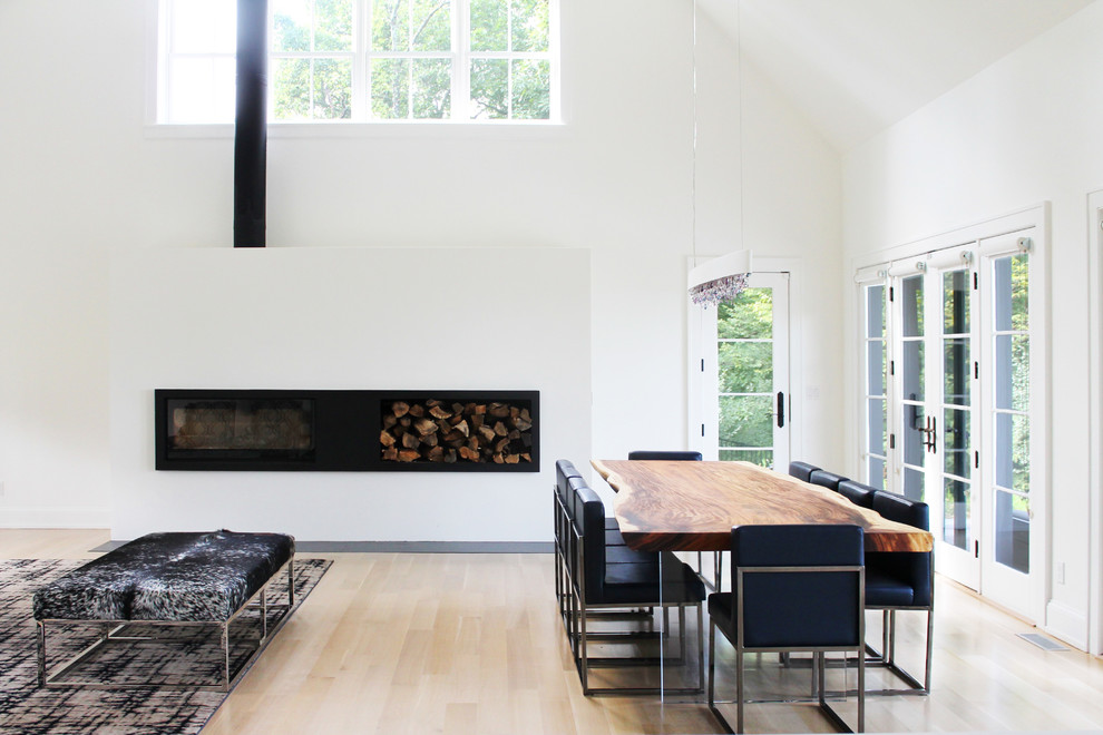 Modelo de comedor minimalista de tamaño medio abierto con paredes blancas, suelo de madera clara, chimenea lineal y marco de chimenea de metal