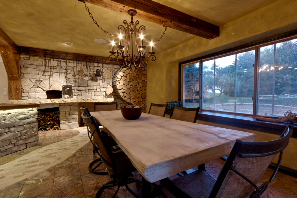 Réalisation d'une grande salle à manger ouverte sur la cuisine chalet avec un mur jaune, un sol en marbre, un poêle à bois et un manteau de cheminée en brique.