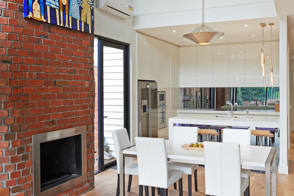 Exemple d'une salle à manger ouverte sur la cuisine tendance de taille moyenne avec un sol en bois brun, un mur blanc, une cheminée standard et un manteau de cheminée en brique.