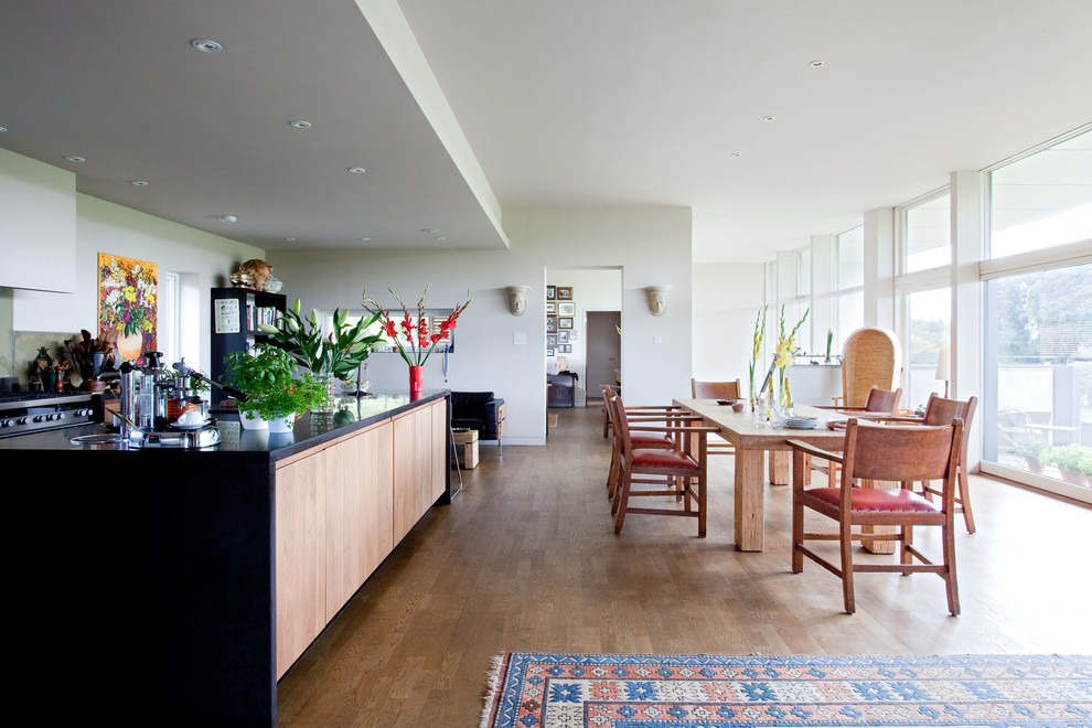 Réalisation d'une grande salle à manger ouverte sur la cuisine design avec un mur blanc et un sol en bois brun.