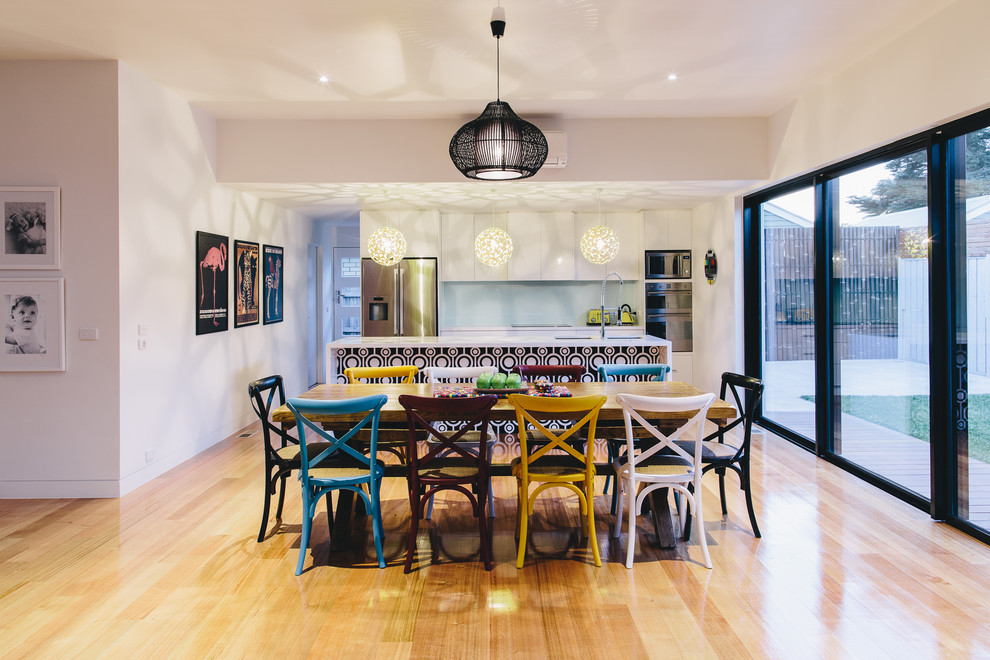 Exemple d'une salle à manger ouverte sur la cuisine éclectique avec un mur blanc et parquet clair.