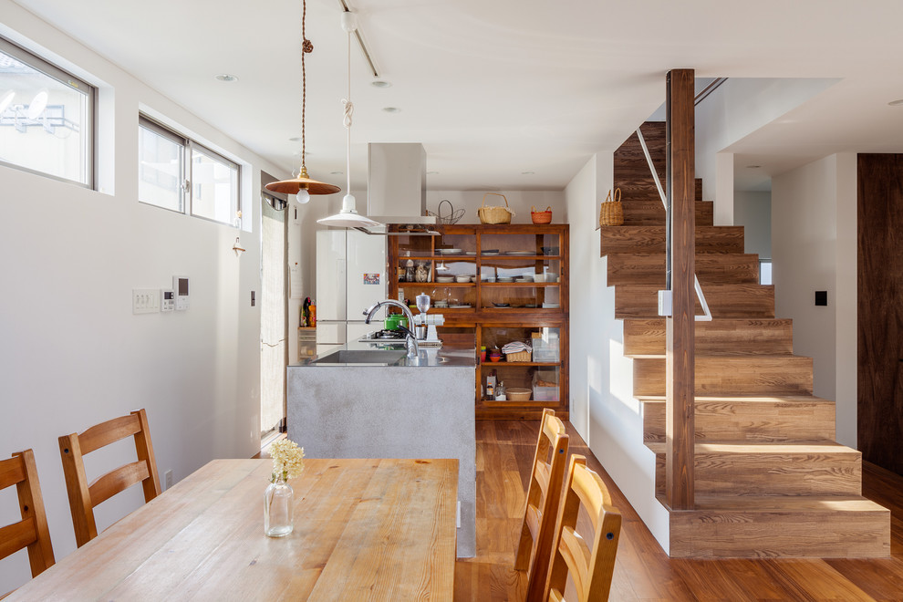 Cette photo montre une petite salle à manger ouverte sur la cuisine nature avec un mur blanc et un sol en bois brun.