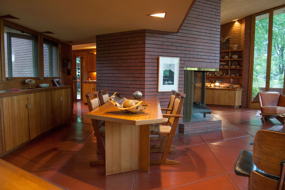 Idée de décoration pour une salle à manger minimaliste avec un manteau de cheminée en brique et un sol rouge.