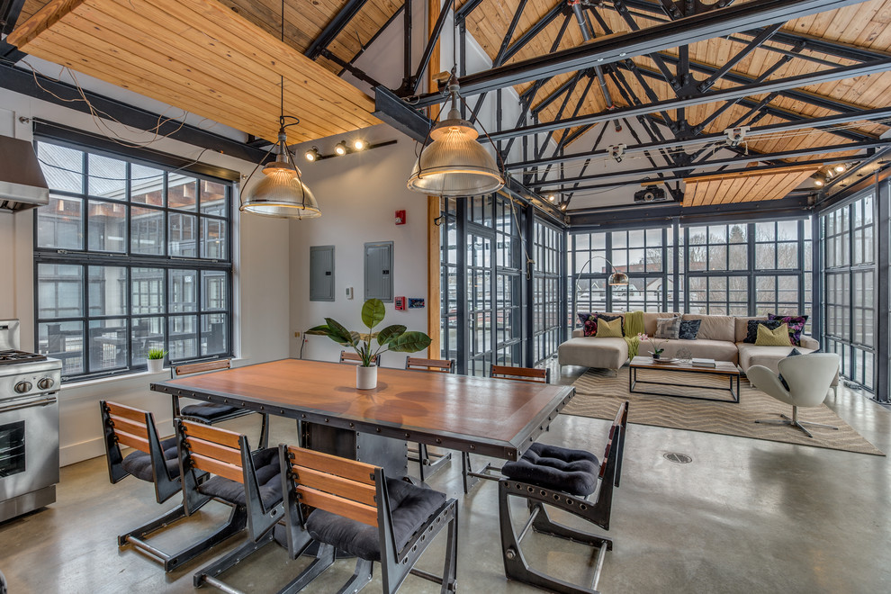 Foto di una sala da pranzo aperta verso il soggiorno industriale con pareti bianche e pavimento in cemento