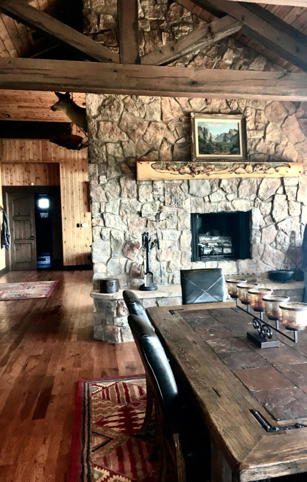 Cette image montre une très grande salle à manger ouverte sur la cuisine chalet avec un mur marron, un sol en bois brun, une cheminée double-face, un manteau de cheminée en pierre et un sol marron.