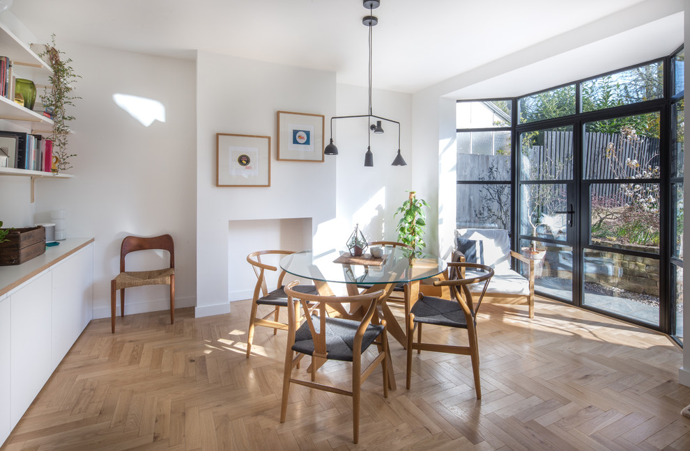 Medium sized scandi kitchen/dining room in West Midlands with white walls, light hardwood flooring, a standard fireplace, a plastered fireplace surround and brown floors.