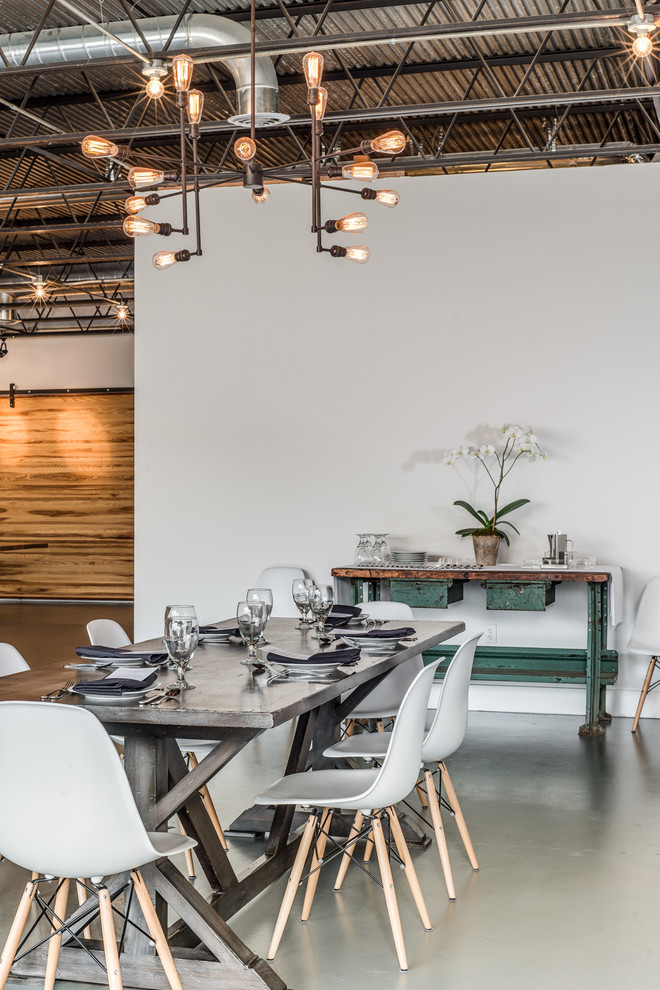 Cette image montre une très grande salle à manger ouverte sur le salon urbaine avec un mur blanc et sol en béton ciré.