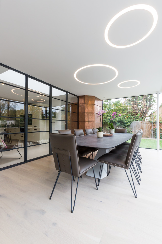 Large contemporary enclosed dining room in London with white walls, light hardwood flooring, no fireplace and beige floors.