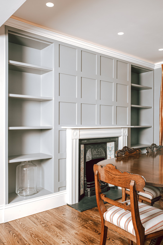 Example of a large classic dark wood floor, brown floor and wall paneling enclosed dining room design in London with gray walls, a standard fireplace and a metal fireplace