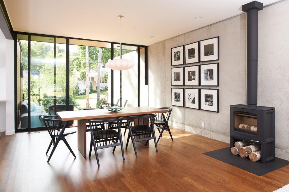 Cette image montre une salle à manger minimaliste avec un sol en bois brun et un poêle à bois.