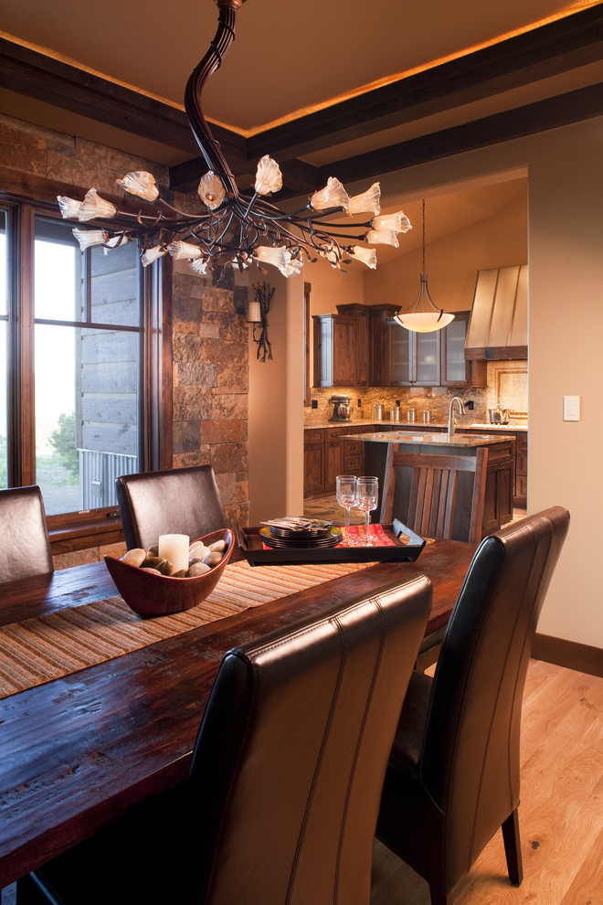 Exemple d'une salle à manger ouverte sur la cuisine montagne de taille moyenne avec un sol en bois brun, un mur beige, une cheminée standard, un manteau de cheminée en pierre et un sol marron.