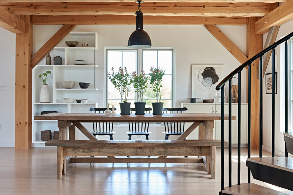 Large farmhouse open plan dining room with white walls, light hardwood flooring and exposed beams.
