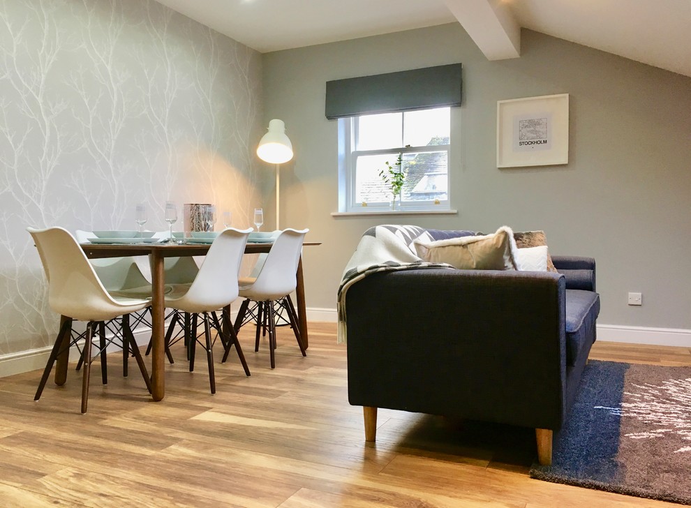На фото: гостиная-столовая среднего размера в скандинавском стиле с серыми стенами, полом из ламината и коричневым полом без камина
