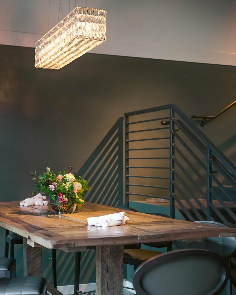 Cette image montre une grande salle à manger ouverte sur la cuisine bohème avec un mur vert, sol en béton ciré, un sol gris, poutres apparentes et du papier peint.