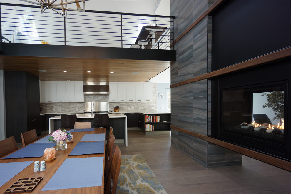Стильный дизайн: гостиная-столовая среднего размера в современном стиле с белыми стенами, темным паркетным полом, двусторонним камином, фасадом камина из металла и коричневым полом - последний тренд