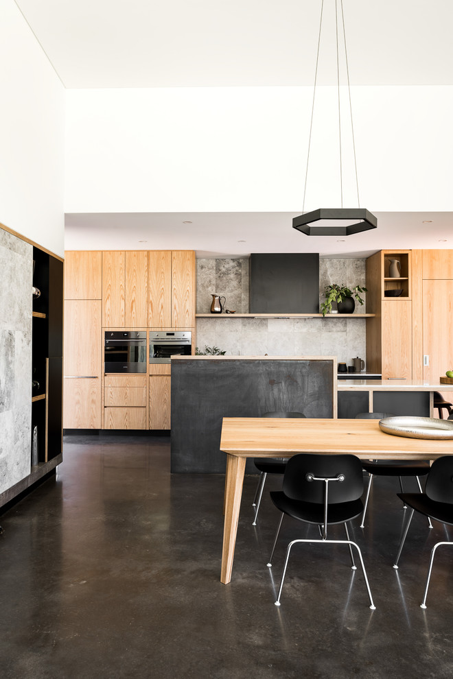 Réalisation d'une salle à manger ouverte sur la cuisine minimaliste avec un mur blanc, sol en béton ciré et un sol noir.
