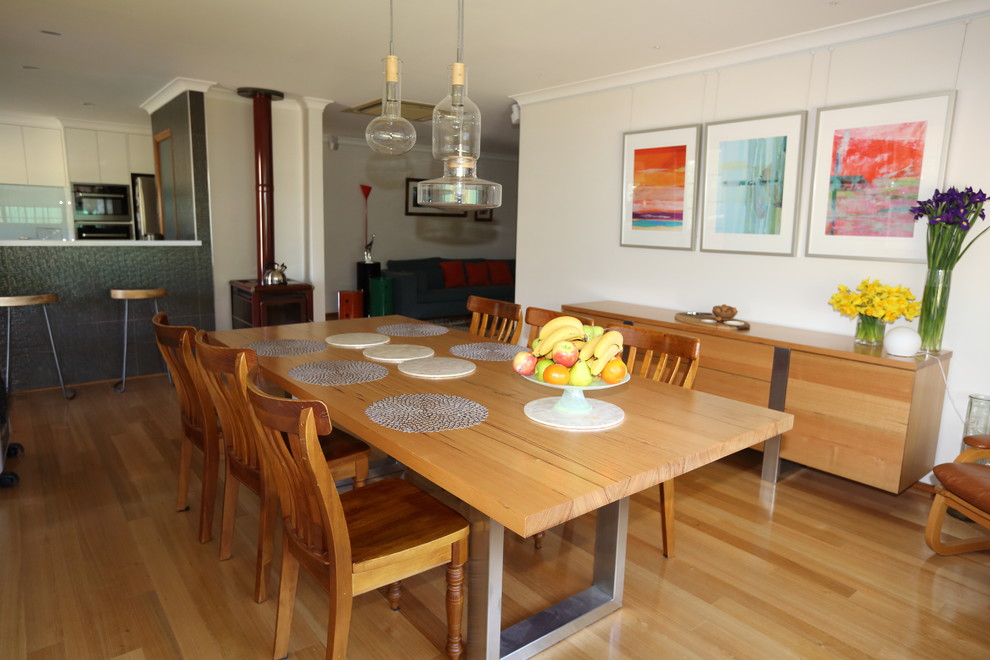 Cette photo montre une grande salle à manger ouverte sur la cuisine tendance avec un mur beige, un sol en bois brun et un poêle à bois.