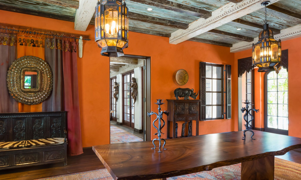 На фото: большая гостиная-столовая в средиземноморском стиле с оранжевыми стенами, темным паркетным полом, стандартным камином, фасадом камина из камня и коричневым полом