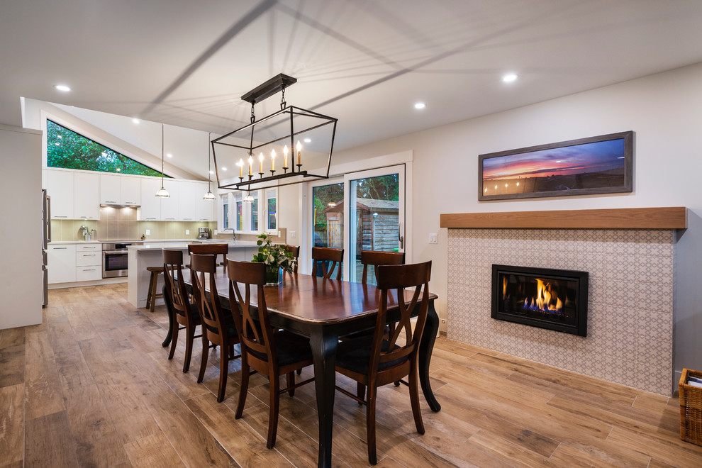 This is an example of a medium sized modern open plan dining room in Other with white walls, medium hardwood flooring, a standard fireplace, a tiled fireplace surround and brown floors.