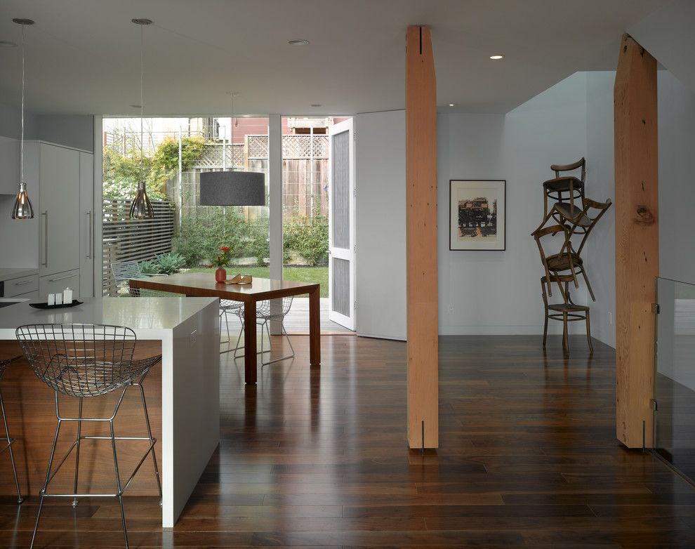Cette image montre une salle à manger ouverte sur la cuisine minimaliste avec un mur blanc et parquet foncé.
