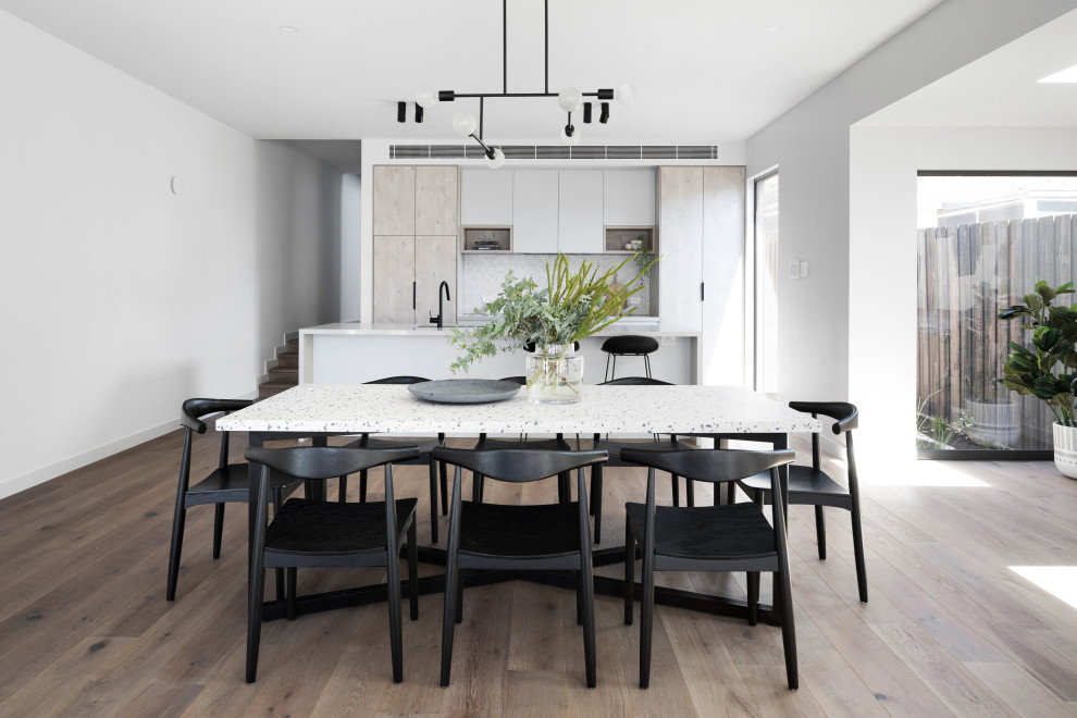 Cette photo montre une salle à manger ouverte sur la cuisine tendance de taille moyenne avec un mur blanc, un sol marron et un sol en bois brun.