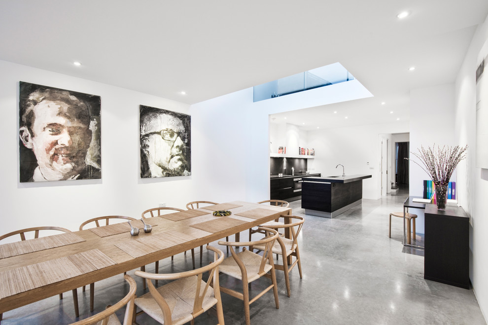 Cette image montre une salle à manger ouverte sur la cuisine design avec un mur blanc et sol en béton ciré.