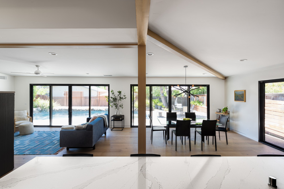 Источник вдохновения для домашнего уюта: гостиная-столовая среднего размера в стиле ретро с белыми стенами, светлым паркетным полом, двусторонним камином, фасадом камина из бетона, коричневым полом и балками на потолке