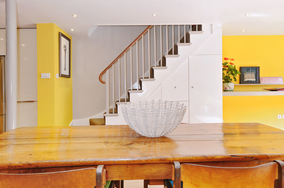 Стильный дизайн: большая кухня-столовая в современном стиле с желтыми стенами, светлым паркетным полом, стандартным камином и фасадом камина из камня - последний тренд