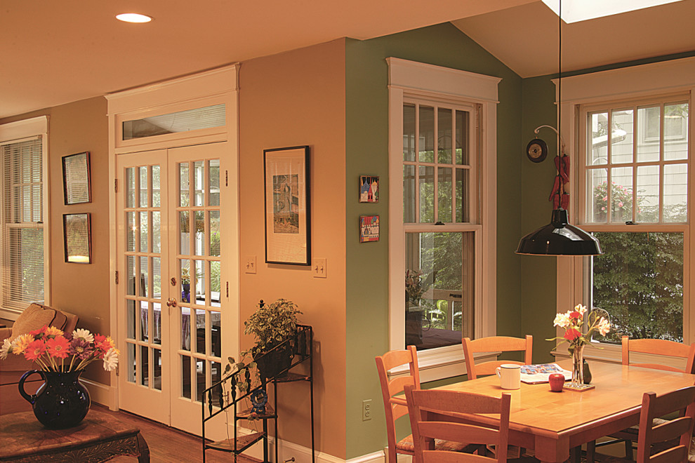 Cette image montre une petite salle à manger ouverte sur la cuisine traditionnelle avec un mur vert, un sol en bois brun, aucune cheminée et un sol marron.