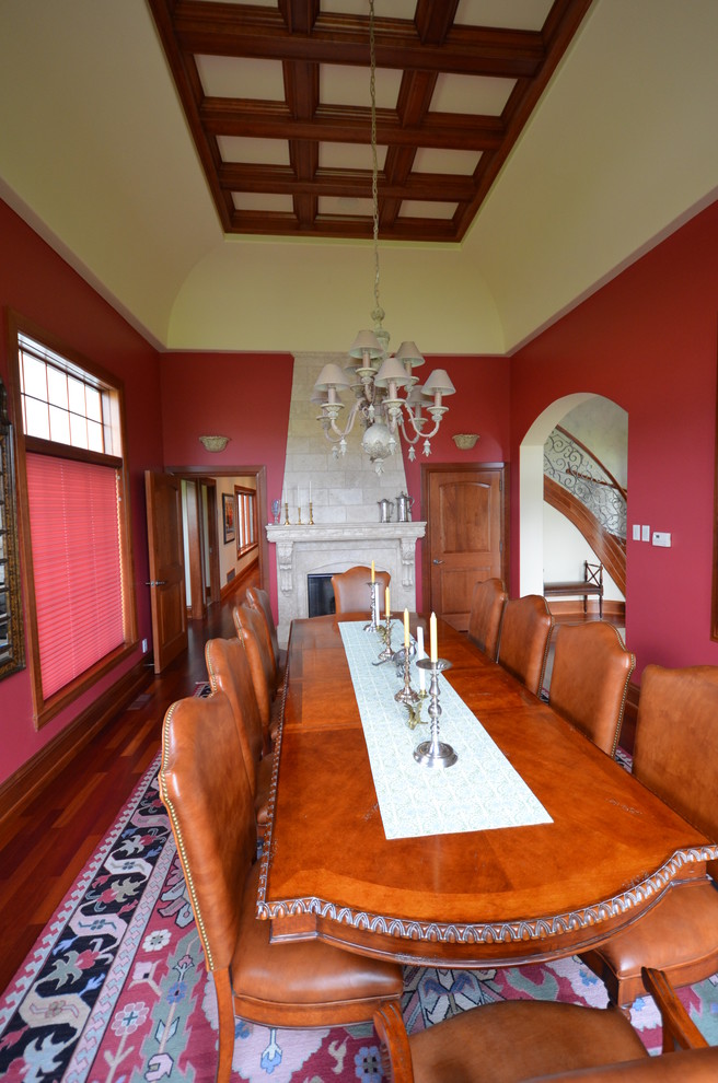 Cette image montre une salle à manger traditionnelle de taille moyenne et fermée avec un mur rouge, parquet foncé, une cheminée standard et un manteau de cheminée en pierre.