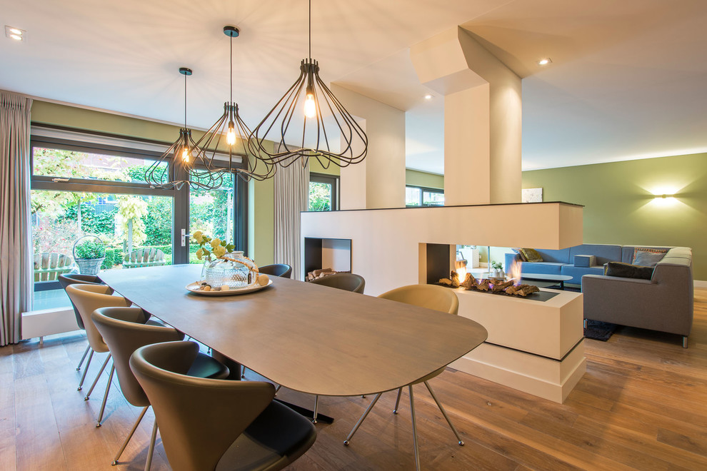 Источник вдохновения для домашнего уюта: гостиная-столовая в современном стиле с зелеными стенами, паркетным полом среднего тона и двусторонним камином