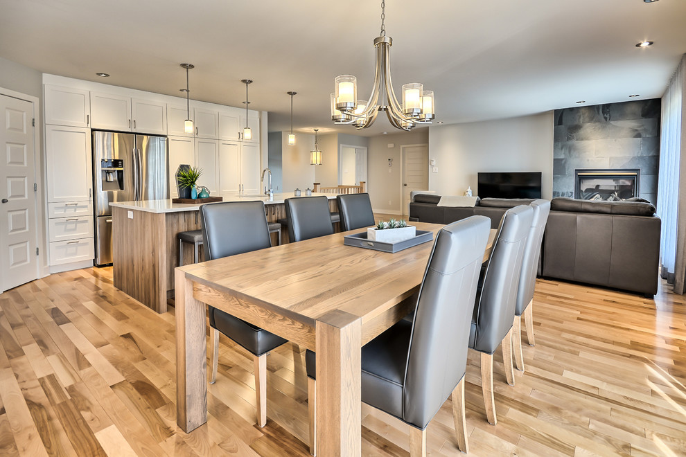 Mittelgroße Moderne Wohnküche mit grauer Wandfarbe, braunem Holzboden, Hängekamin, Kaminumrandung aus Stein und braunem Boden in Montreal