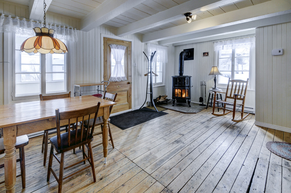 Cette image montre une petite salle à manger ouverte sur la cuisine chalet avec un mur blanc, parquet clair, un poêle à bois et un manteau de cheminée en carrelage.