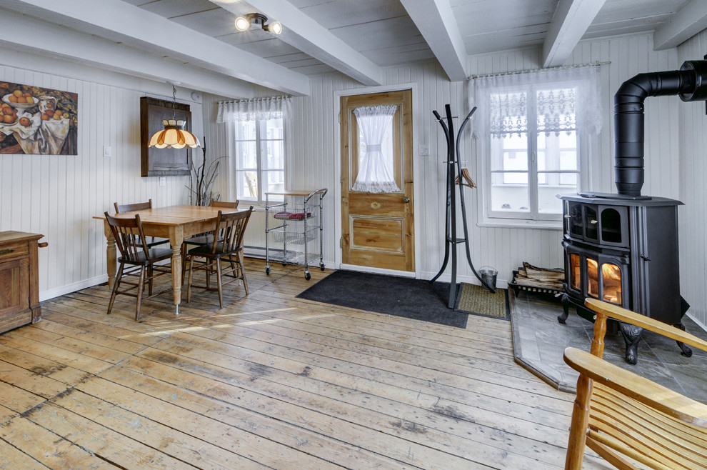 Cette photo montre une petite salle à manger ouverte sur la cuisine montagne avec un mur blanc, parquet clair, un poêle à bois et un manteau de cheminée en carrelage.
