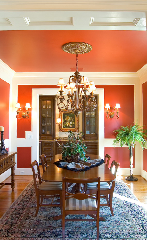 Cette image montre une salle à manger traditionnelle avec un mur rouge et un sol en bois brun.