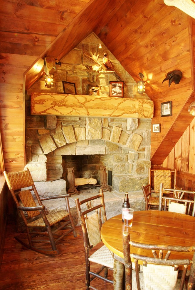 Cette image montre une petite salle à manger chalet fermée avec une cheminée standard, un manteau de cheminée en pierre, un sol en bois brun et un sol marron.