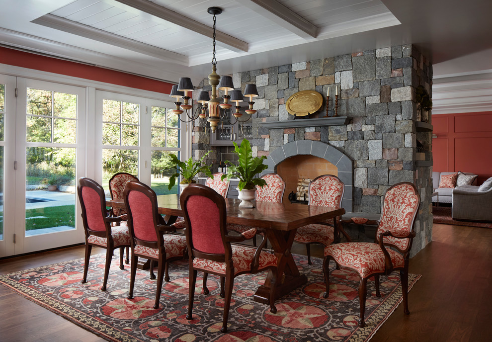 Cette image montre une salle à manger traditionnelle avec un mur orange, parquet foncé, une cheminée standard et un manteau de cheminée en pierre.