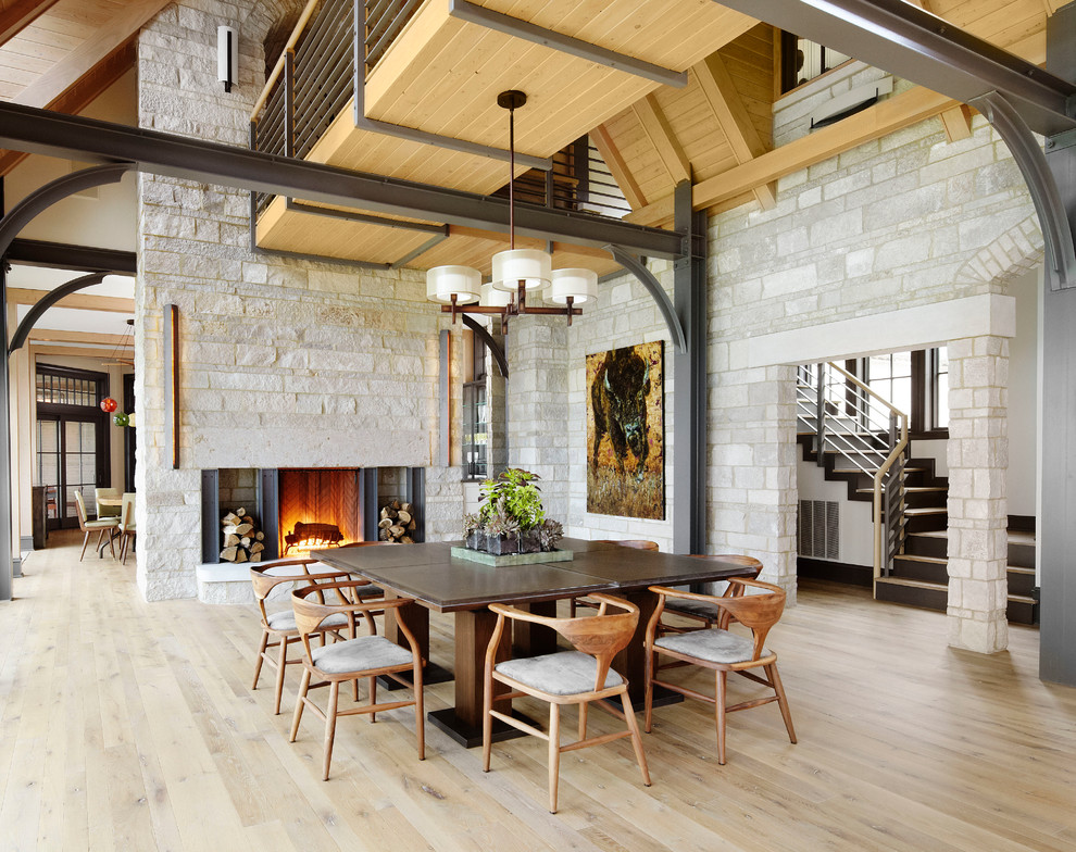 Cette image montre une salle à manger design avec un sol en bois brun, une cheminée standard et un manteau de cheminée en pierre.