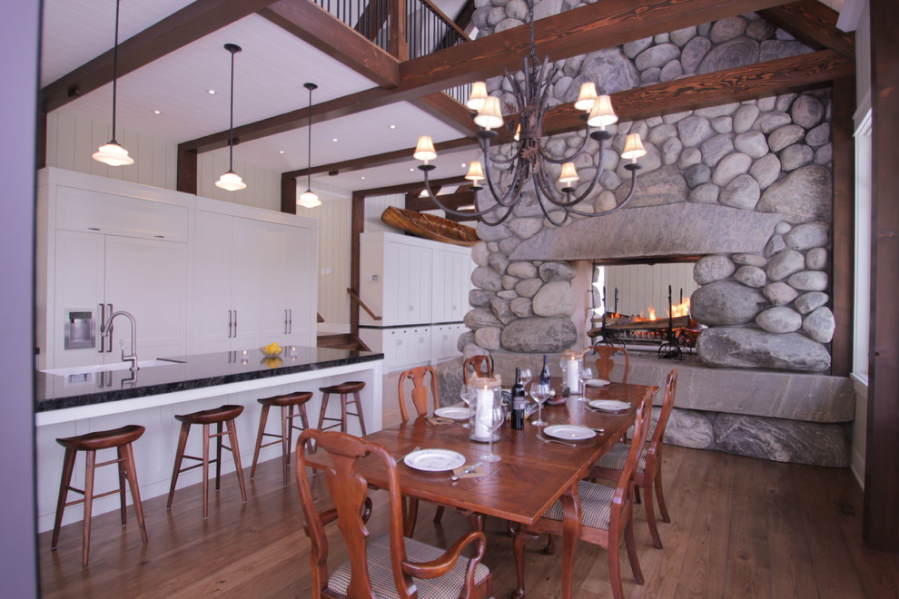 Kitchen/dining room combo - large rustic medium tone wood floor kitchen/dining room combo idea in Toronto with a two-sided fireplace and a stone fireplace