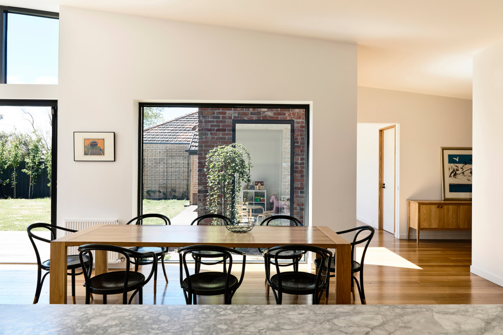 Immagine di una sala da pranzo aperta verso il soggiorno minimal con pareti bianche, pavimento in legno massello medio, pavimento marrone e soffitto a volta
