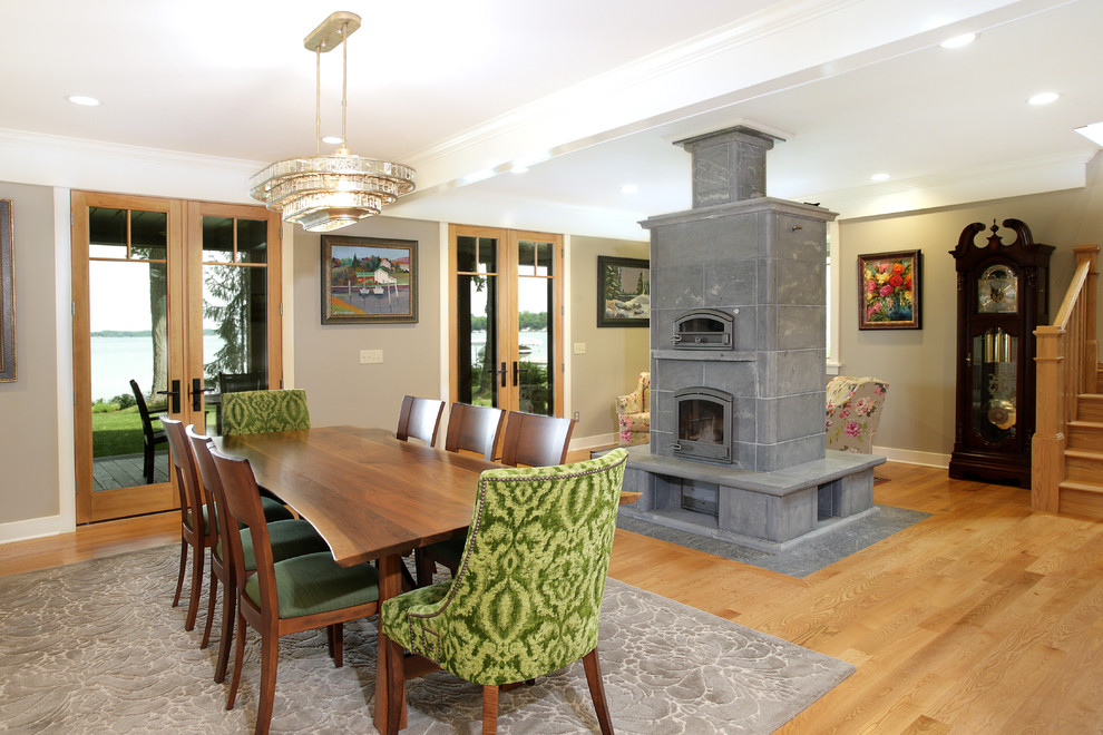 Idée de décoration pour une salle à manger ouverte sur le salon craftsman avec un mur gris, parquet clair, une cheminée standard, un manteau de cheminée en carrelage et un sol marron.
