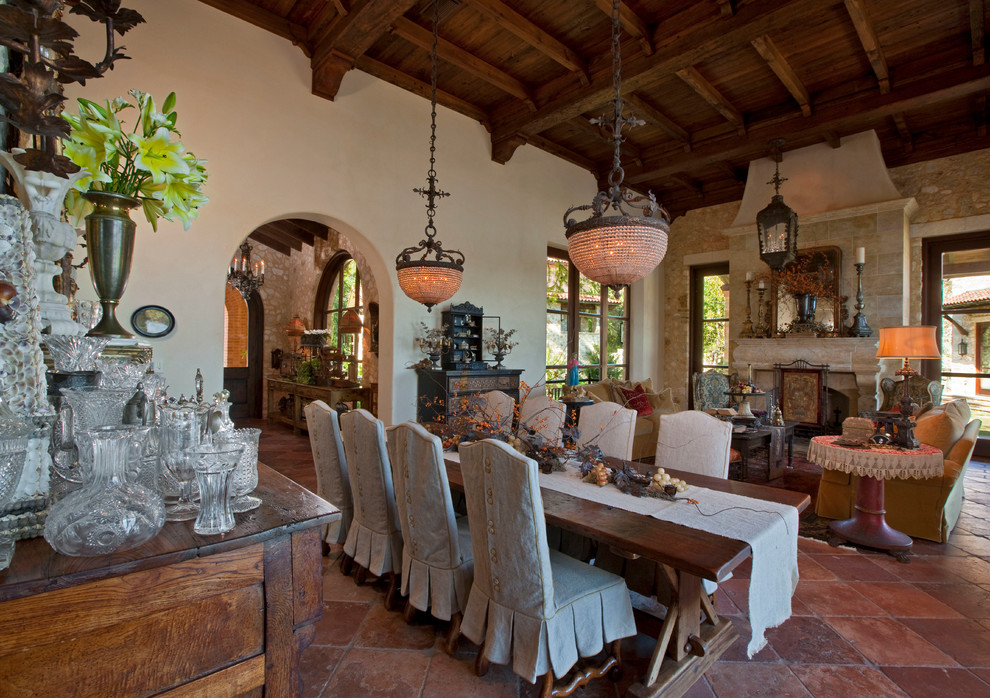 Exemple d'une grande salle à manger ouverte sur le salon méditerranéenne avec un mur blanc, tomettes au sol, une cheminée standard et éclairage.