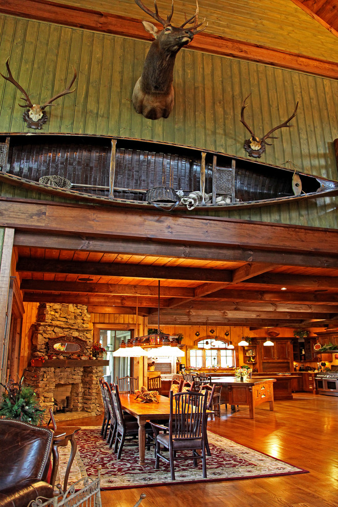 Cette image montre une grande salle à manger ouverte sur la cuisine chalet avec un mur marron, un sol en bois brun, une cheminée d'angle et un manteau de cheminée en pierre.