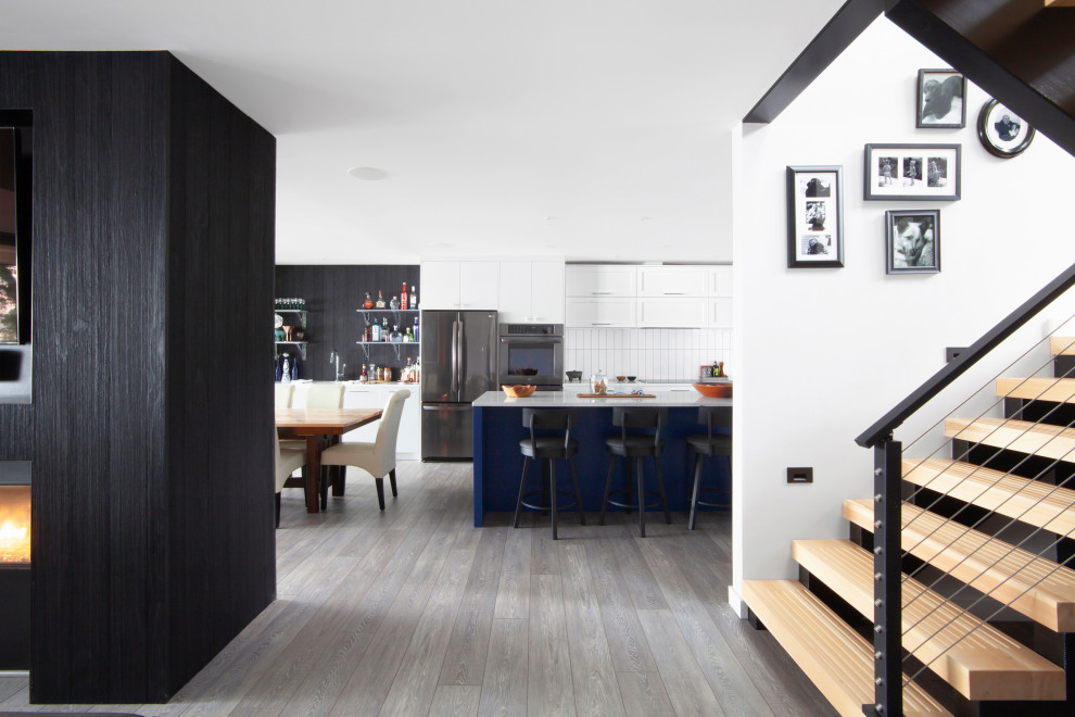 На фото: кухня-столовая среднего размера в стиле модернизм с белыми стенами, полом из винила, двусторонним камином, фасадом камина из дерева, серым полом и деревянными стенами