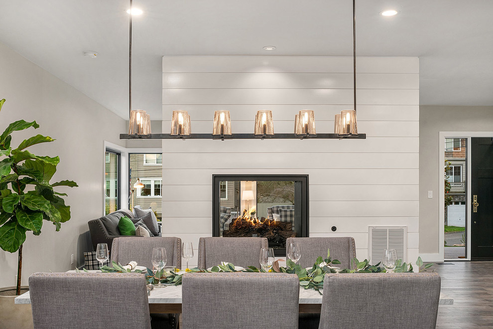 Réalisation d'une salle à manger ouverte sur le salon champêtre de taille moyenne avec un mur gris, un sol en bois brun, une cheminée double-face, un manteau de cheminée en bois et un sol gris.