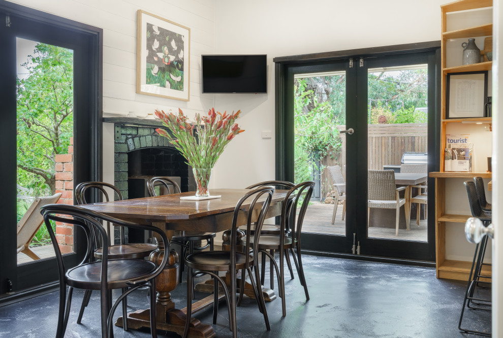 This is an example of a traditional kitchen/dining room in Melbourne with white walls, a wood burning stove, a brick fireplace surround and black floors.