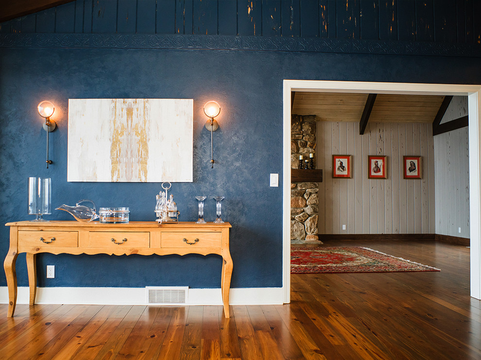 Modelo de comedor tradicional renovado grande abierto con paredes azules, suelo de madera en tonos medios, todas las chimeneas y marco de chimenea de piedra