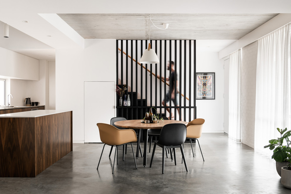 Immagine di una sala da pranzo aperta verso la cucina contemporanea con pareti bianche, pavimento in cemento e pavimento grigio
