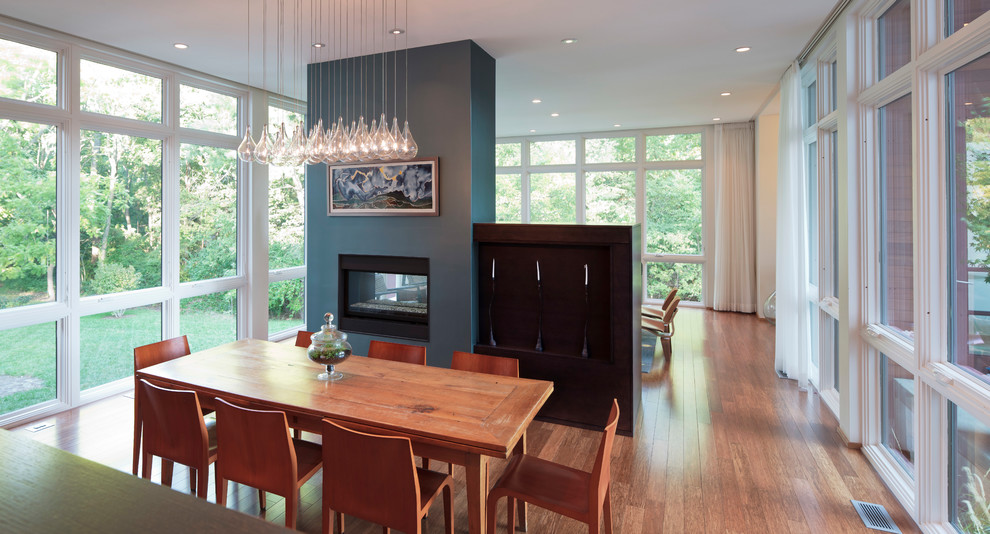 Cette photo montre une salle à manger ouverte sur la cuisine avec un mur blanc, parquet en bambou et une cheminée double-face.